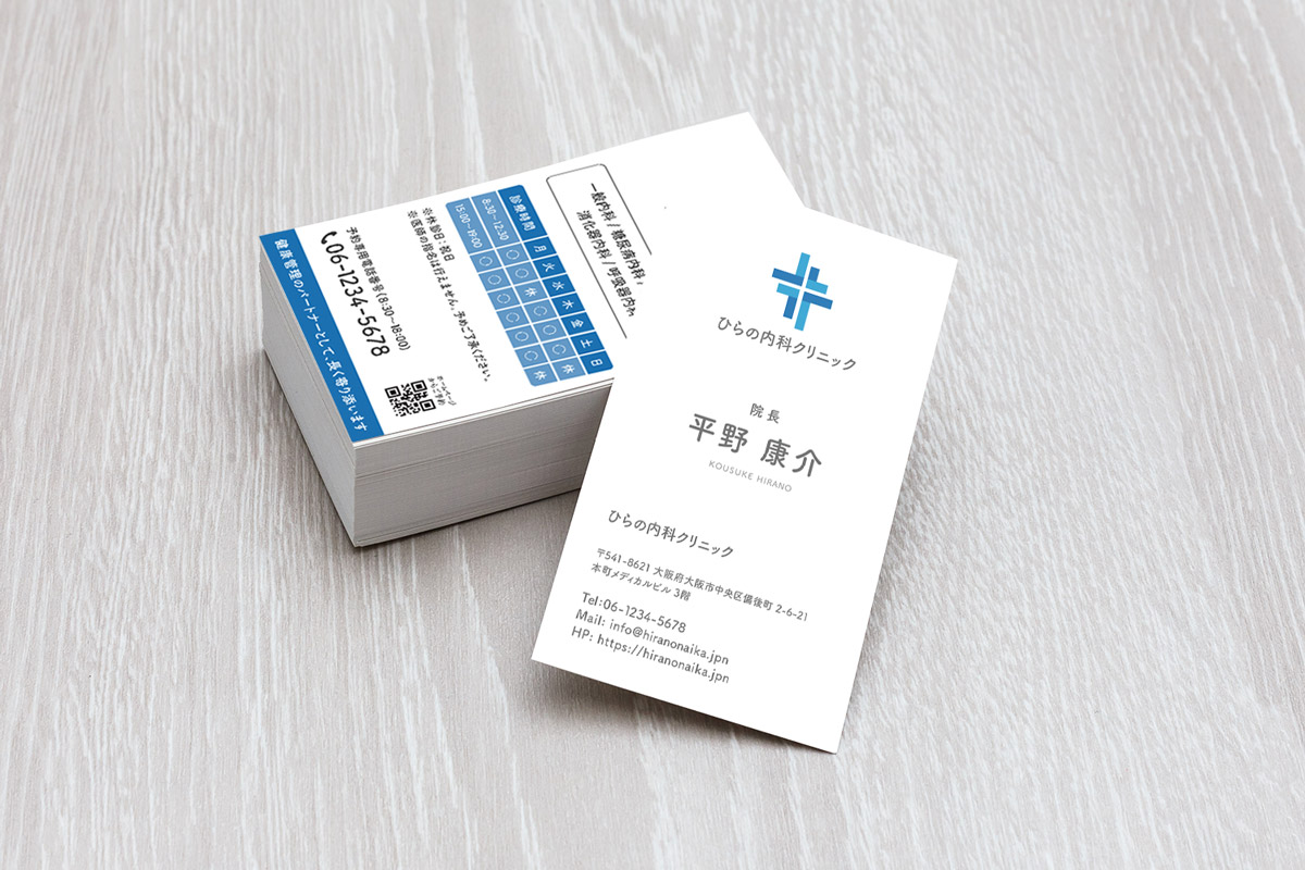 印刷されたひらの内科クリニック名刺の写真。名刺の束と1枚を木目テーブルに置いた仕上がりイメージ