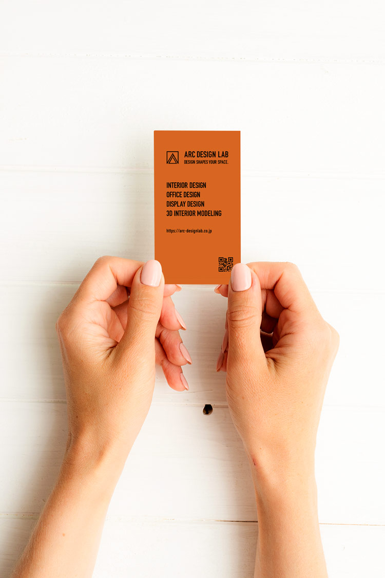 インテリアデザイン事務所名刺の裏面を手に持つイメージ写真｜ブランドカラーのテラコッタが印象を強めるスタイリッシュなデザイン